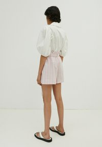 Weißes Shirt mit Puffärmeln, rosa gestreifte hochgeschnittene Shorts und schwarze Sandalen. Glatte Texturen; lockere Passform; auffälliges Gürtel-Detail an den Shorts.