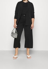 Blazer nero su un top nero, abbinato a pantaloni neri con gamba larga. Accentuato da una borsa a tracolla patterned bianco e nero e sandali bianchi a pianta spessa.
