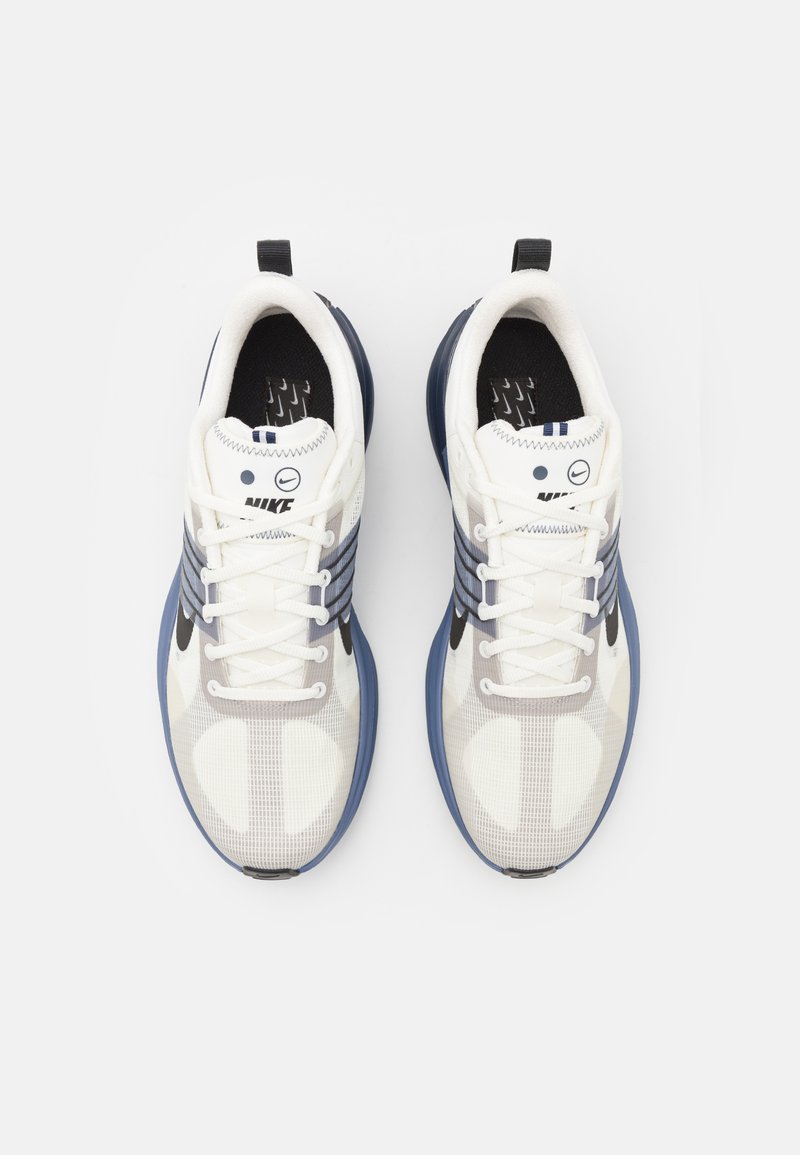 Zapatillas Nike de malla blanca con acentos en azul oscuro, que presentan tres rayas en azul oscuro, cordones redondos y suelas texturizadas.