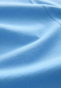 Helleblaue Baumwollstoffe mit glatter Textur, die subtile Falten und ein gleichmäßiges Webmuster aufweisen, betonen Weichheit und Komfort.