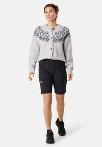 Ljusgrå ullkofta med blåmönstrad ok, träknappar; ihop med svarta cargoshorts med dragkedjefickor, bärs med svarta skor.