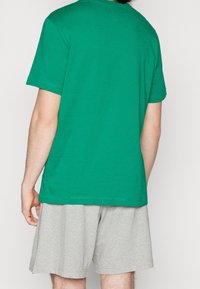 Grön bomullströja med korta ärmar, med rund halsringning. Matchas med ljusgrå shorts, vilket ger en avslappnad passform och mjuk textur.