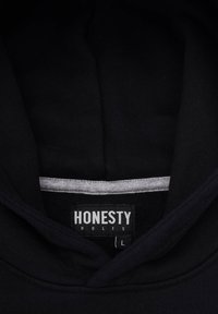 Svart hoodie med en randig krage, med en etikett som visar "ÄRLIGHET ÄR REGELN" och storlek "L" synlig inuti halsringningen. Mjuk, texturerad tyg.