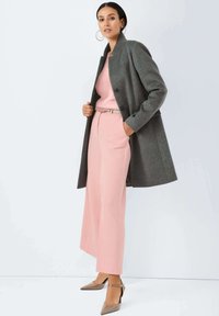 Grijze wolkenjas, roze trui, lichtroze wijde broek en beige puntige hakken met enkelbandje. Circulaire oorbellen completeren de look.
