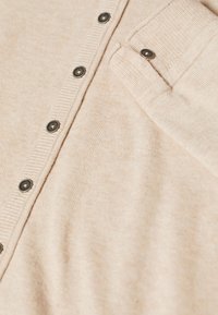 Light beige cardigan made of soft knit fabric. Features a row of dark buttons, ribbed cuffs, and a pocket detail on the chest.