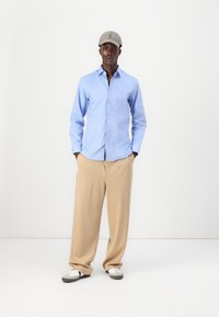 Camisa azul claro de botones, pantalones de pierna ancha beige, gorra gris y zapatos bicolores. Tejido suave con un ajuste entallado y un sutil brillo.