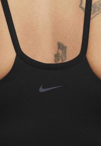 Black athletic sports bra with a smooth texture, thin straps, and a small gray Nike logo on the front.