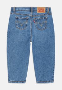 Modre kavbojke z visokim pasom, dvema zadnjima žepoma z rumenim šivi, Levi's rdeča oznaka in usnjena oznaka blagovne znamke na pasu.