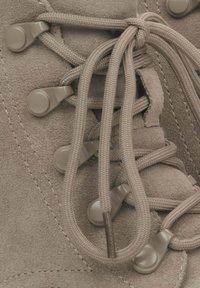 Jasnobrązowe, zamszowe buty trekkingowe z okrągłymi sznurowadłami i plastikowymi oczkami. Posiadają teksturowaną cholewkę oraz wzmocnione szwy dla większej trwałości.