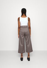 Breda byxor med mönster i bruna nyanser. Elastisk midja, texturerad tyg, i kombination med en vit linne och svarta blockklackskor.