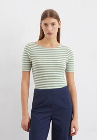 Grün-weiß gestreiftes Kurzarm-T-Shirt mit weitem Ausschnitt, kombiniert mit navyblauen hoch taillierten Hosen, die eine figurbetonte Silhouette bieten.