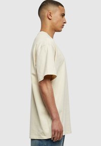 Beige bomull t-skjorte med korte ermer, løs passform, rund hals og sidestykker. Bærer den sammen med blå denim jeans, vist mot en nøytral bakgrunn.