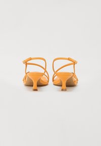 Sandales à talons hauts jaunes avec des brides fines à la cheville, un plateau moulé et un petit talon évasé. Texture en cuir lisse et mat.