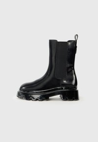 Botines de charol negro con paneles laterales elásticos, suela de goma gruesa y tirador en la parte trasera para ponerlos y quitarlos con facilidad.