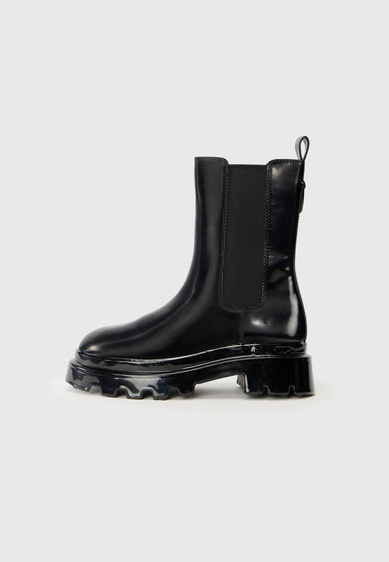 Botines de charol negro con paneles laterales elásticos, suela de goma gruesa y tirador en la parte trasera para ponerlos y quitarlos con facilidad.