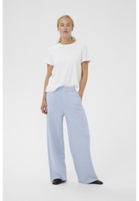 Weißes T-Shirt mit kurzen Ärmeln kombiniert mit weitem, hellblauem Jogginghose. Die Hose hat eine glatte Textur und einen elastischen Bund.