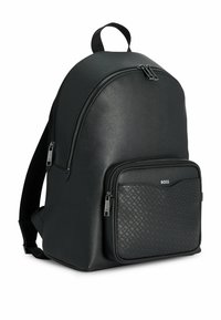 Zaino in pelle nera con una tasca frontale texturizzata, chiusure a zip doppie e spallacci imbottiti. Dettaglio logo discreto sul davanti.