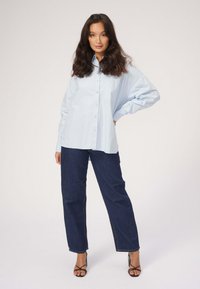 Lyseblå skjorte med lange ærmer, parret med mørkeblå højtaljede jeans. Sko med stropper i træfarve fuldender outfittet.