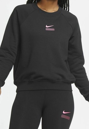 Ensemble sweat noir et leggings avec logos Nike swoosh rose et motifs en grille porté par une personne aux cheveux tressés.
