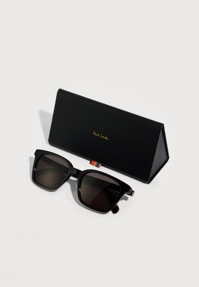 Μαύρα γυαλιά ηλίου με σκούρους φακούς, τετράγωνο πλαίσιο και διακοσμητικές πλευρικές λεπτομέρειες. Συνοδεύονται από μαύρη δερμάτινη θήκη με χρυσό λογότυπο.