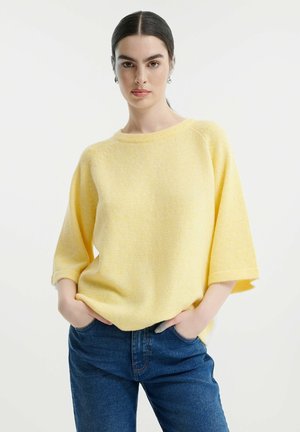 Yellow, textured knit sweater with a round neckline and wide sleeves, paired with blue jeans. Simple design and soft fabric.