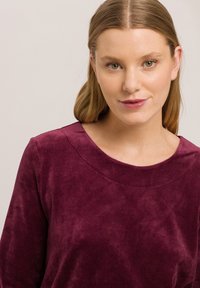 Top de terciopelo burdeos con escote redondo y mangas largas. Textura suave con un brillo sutil y costuras lisas.