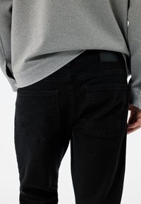 Czarne dżinsy o slim fit, z dwiema tylnymi kieszeniami, gładką teksturą oraz czarną metką na pasku.