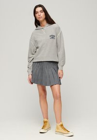 Felpa grigia con un logo, abbinata a una gonna plissettata in bianco e nero a quadretti. Completata con sneakers alte gialle.