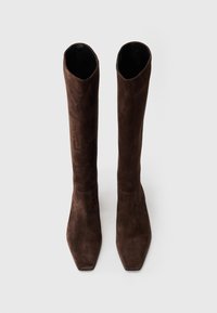 Bottes en cuir suédé marron hauteur genou avec un design à bout carré. La texture lisse présente des accents de coutures près de la cheville.