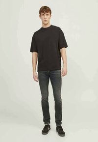 Μαύρη μπλούζα με κοντά μανίκια και άνετη εφαρμογή, συνδυασμένη με σκούρα τζιν. Το μοντέλο στέκεται σε ουδέτερο φόντο, φορώντας μαύρα αθλητικά παπούτσια.