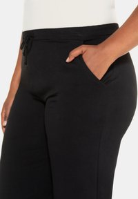 Pantaloni jogger neri realizzati in tessuto morbido, dotati di vita regolabile con cordino e tasche laterali. Texture liscia con un design aderente.