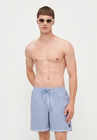 Šviesiai mėlyni maudymosi šortai su raišteliu juosmens srityje, pagaminti iš švelnios medžiagos. Kairėje pusėje yra logotipo lopas.