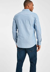 Helles blaugraues Chambray-Hemd mit langen Ärmeln und Knopfmanschetten, gerade geschnitten und mit einem kleinen Kragen, kombiniert mit dunklen Denim-Jeans.