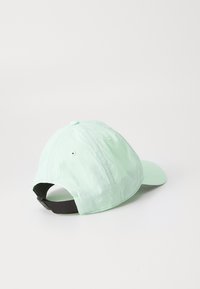 Cască de baseball verde deschis cu curea ajustabilă neagră, văzută din spate pe o suprafață albă simplă.