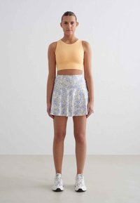 Hellorange Cropped-Top, kombiniert mit einem Blumenkleid in Pastellblau- und Gelbtönen. Weiße Sportschuhe runden das Outfit ab.