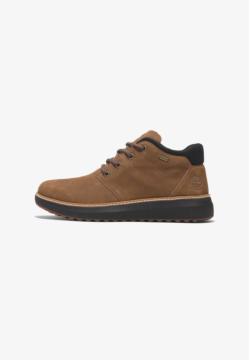 Brown suede shoes with black accents, lace-up design, padded collar, and textured rubber sole, featuring a stitched detail and logo.