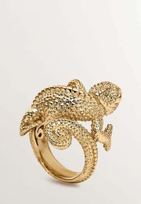 Anillo dorado con forma de camaleón texturizado, que presenta detalles intrincados y un diseño de cola en espiral, proporcionando un efecto tridimensional.