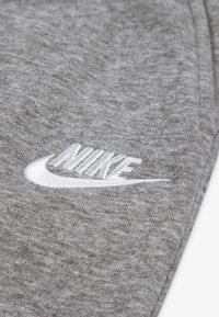 Material dintr-un hanorac gri cu o textură moale, având un logo Nike alb brodat. Accent pe designul distinctiv swoosh al logo-ului.