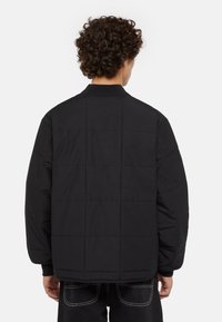 Černá péřová bunda s prošívaným designem, s vystuženým límcem a žebrovanými manžetami. Hladká textura a oversized střih.