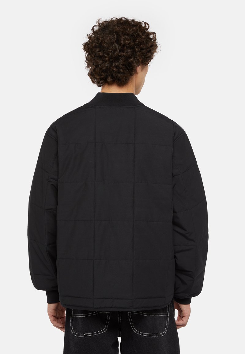 Doudoune noire avec un design matelassé, dotée d'un col montant et de poignets côtelés. Texture lisse et coupe oversize.