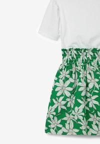 Vit kortärmad topp som är fäst vid en grön kjol med vita blommönster. Kjolen har en elastisk midja för komfort.