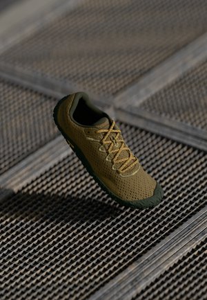 Lekki, siateczkowy but sportowy w oliwkowym zielonym i beżowym kolorze, z teksturowanym cholewką, kontrastującymi sznurowadłami oraz elastyczną, wzorzystą podeszwą.
