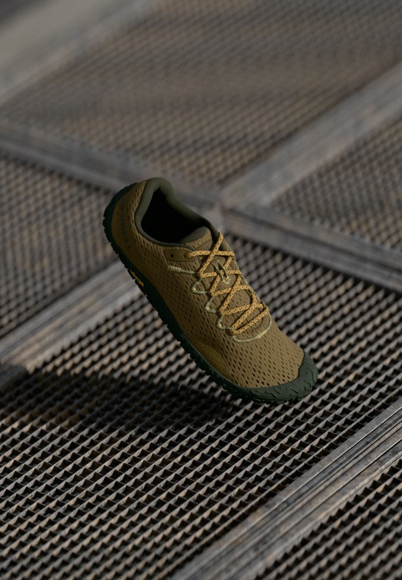 Zapatilla atlética ligera de malla en verde oliva y beige, con parte superior texturizada, cordones en contraste y suela flexible con un patrón.