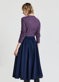 Lila Strickpullover mit langen Ärmeln, getragen mit einem marineblauen plissierten Rock. Das Outfit hat eine taillierte Passform und eine fließende Silhouette.