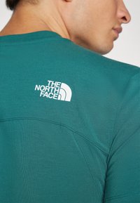 Turkusowa koszulka z krótkim rękawem, wykonana z miękkiego materiału, z okrągłym dekoltem, z białym logo "The North Face" na górnej części pleców.