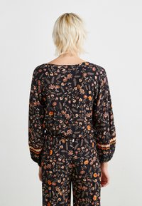 Blouse à manches longues noire avec un motif floral multicolore, des poignets élastiques froncés et une coupe décontractée, avec une bande accentuée à l'ourlet.