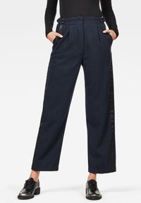 Mörkblå byxor med vida ben, framveck och svarta satinsidostråk. Har knappdetaljer i midjan.