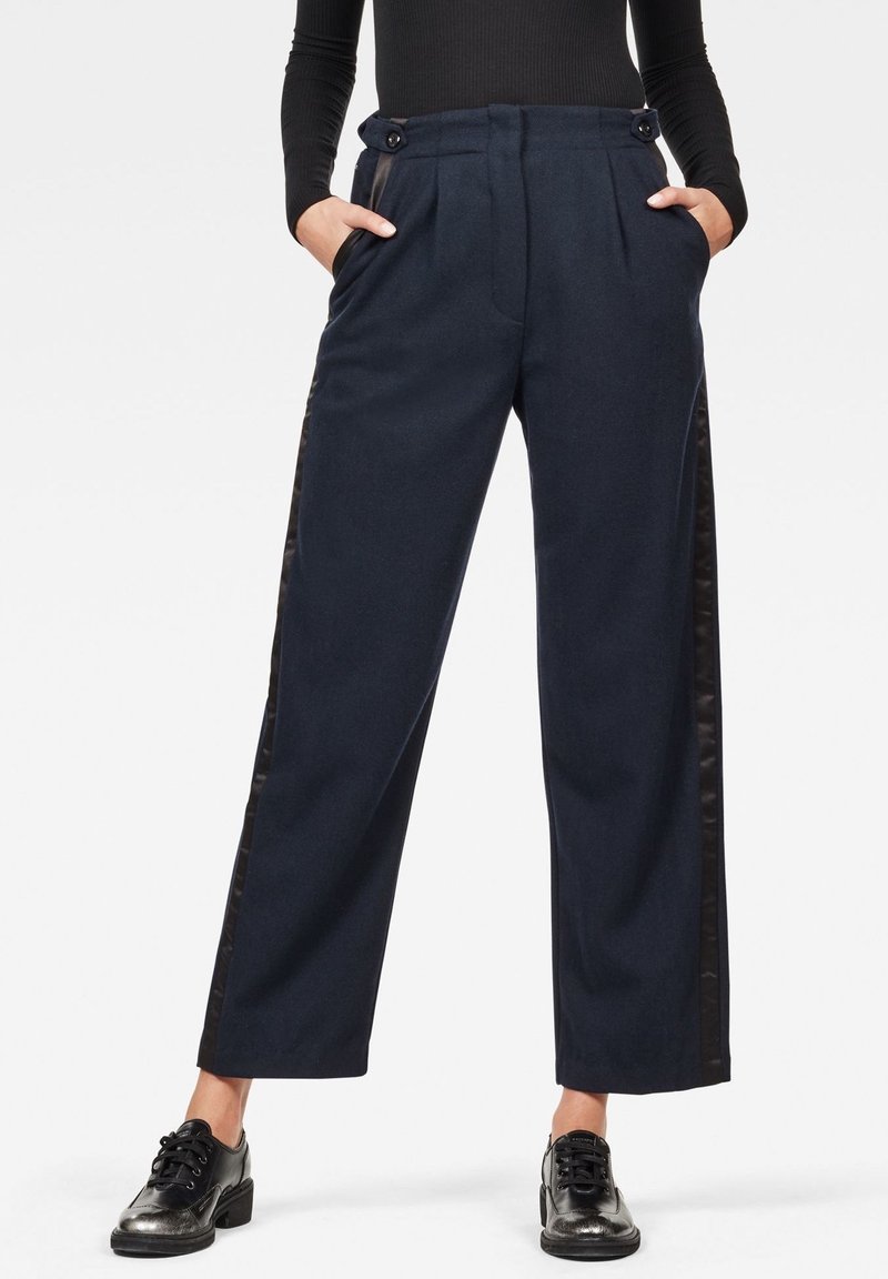 Mörkblå byxor med vida ben, framveck och svarta satinsidostråk. Har knappdetaljer i midjan.