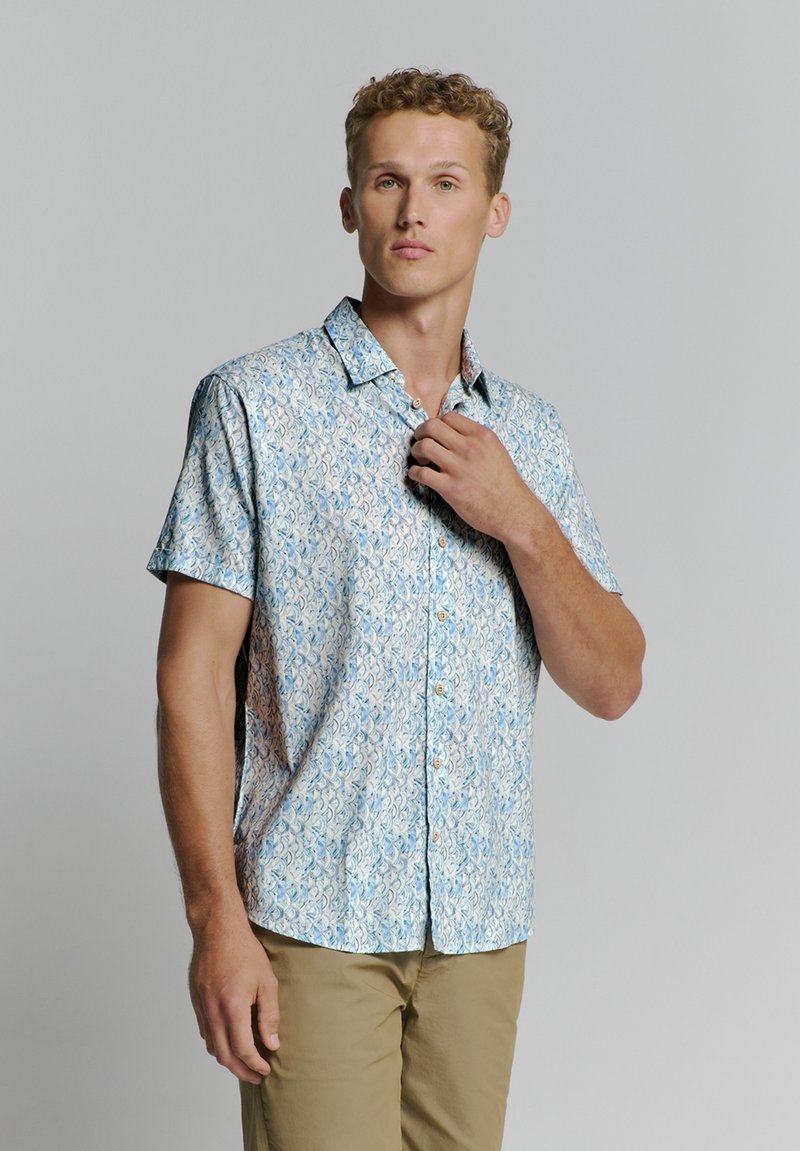 Korte mouwen shirt in lichtblauw met een paisleypatroon, met een button-down kraag en tan knopen, gecombineerd met beige broeken.