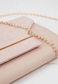 Růžové koženkové psaníčko s texturovaným povrchem, vybavené zlatým řetízkovým popruhem a kovovým proužkem jako ozdobou na přední klopě.